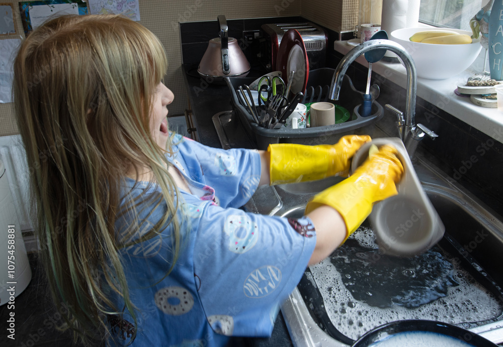 Child (8-9 years old) in Yellow marigold gloves washing up inside kitchen during day cleaning cat bowl