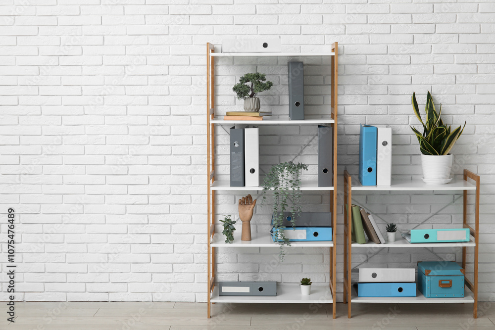 Shelf units with document folders and plants near white brick wall in office Shelf units with document folders and plants near white brick wall in office