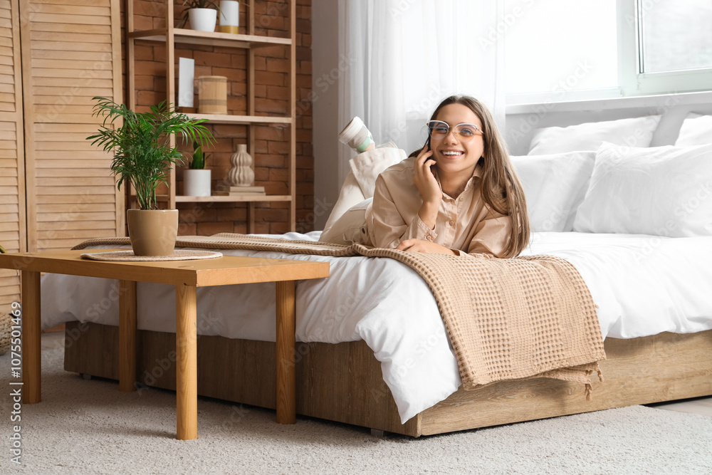 Obraz premium Pretty young woman talking by phone on bed in light bedroom
