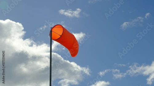 Wind blowing red windsock that is showing the direction and strength of the wind at the airfield against blue sky and white clouds during daytime