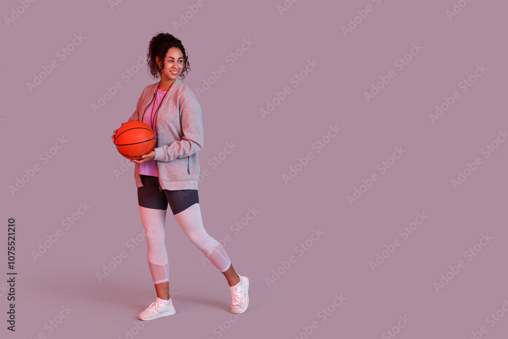 Female African-American basketball trainer with ball on pink background Female African-American basketball trainer with ball on pink background