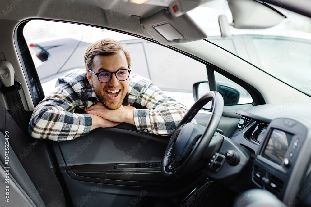 Young man looking through window inside new car, checking it before purchase at modern dealership store. Cheerful guy buying or renting automobile at showroom Young man looking through window inside new car, checking it before purchase at modern dealership store. Cheerful guy buying or renting automobile at showroom