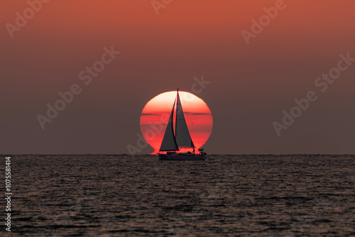 Sailboat passing in front of the sun at sunset