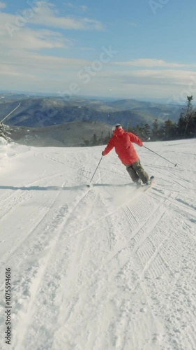 Vertical video 4K of man alpine snow skiing down a snowy ski slope on a mountain on a cold winter day with the sunshine and blue sky. Thrill and extreme sports activity.