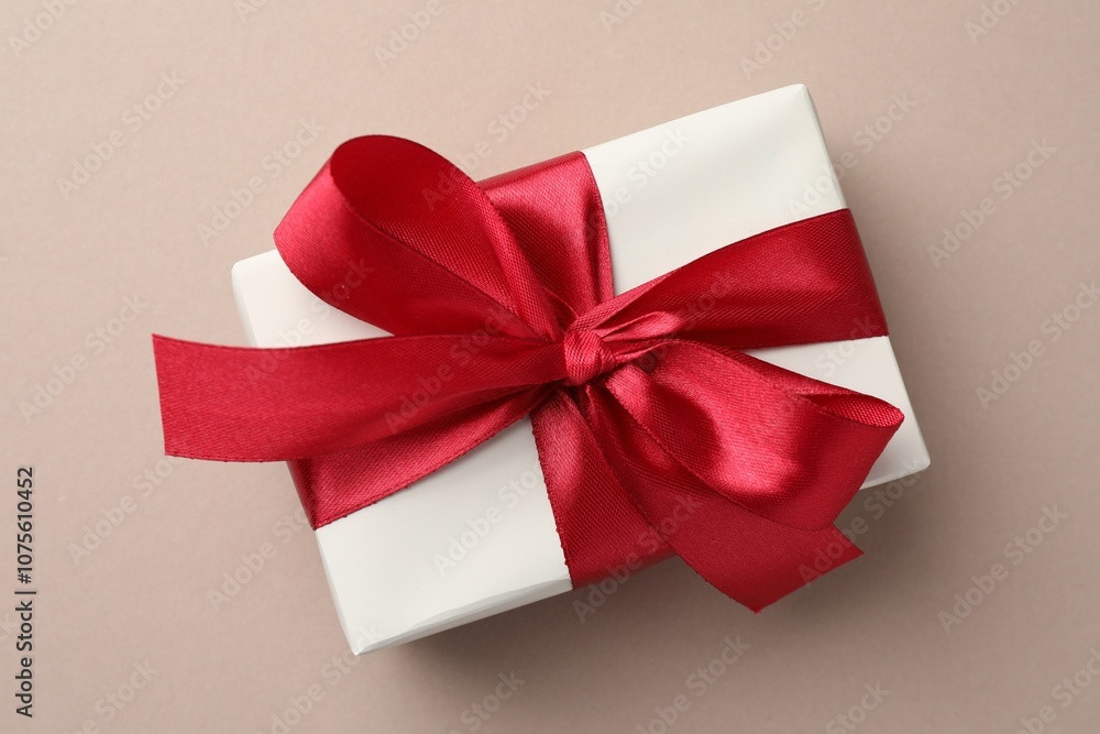 Gift box with red bow on beige background, top view Gift box with red bow on beige background, top view