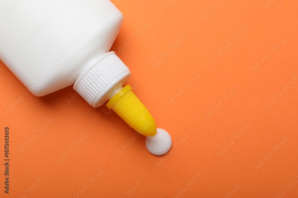 Bottle of glue on orange background, top view. Space for text Bottle of glue on orange background, top view. Space for text