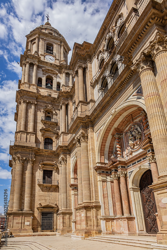 Fototapeta premium Fragments of majestic facade of Malaga Cathedral (1782), Baroque and Renaissance architecture with grand columns, detailed carvings, and archways under a clear blue sky. Malaga, Andalusia, Spain.