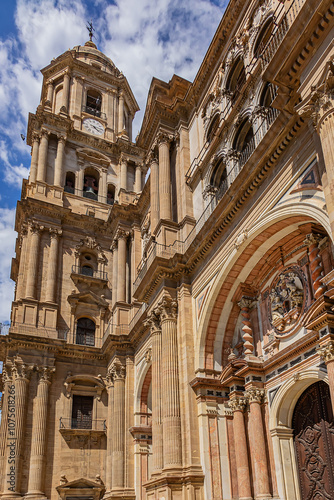 Fragments of majestic facade of Malaga Cathedral (1782), Baroque and Renaissance architecture with grand columns, detailed carvings, and archways under a clear blue sky. Malaga, Andalusia, Spain. photo