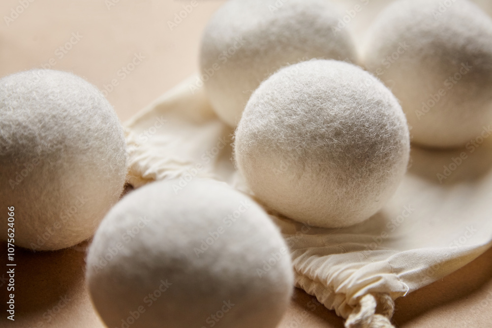Close-up of soft white wool dryer balls resting on an open cotton drawstring bag, set against a warm, neutral background. Ideal for eco-friendly laundry Close-up of soft white wool dryer balls resting on an open cotton drawstring bag, set against a warm, neutral background. Ideal for eco-friendly laundry