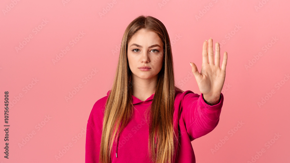 Stop gesture. Strict teenage girl in pink hoodie raises hand, studio shot, free space Stop gesture. Strict teenage girl in pink hoodie raises hand, studio shot, free space
