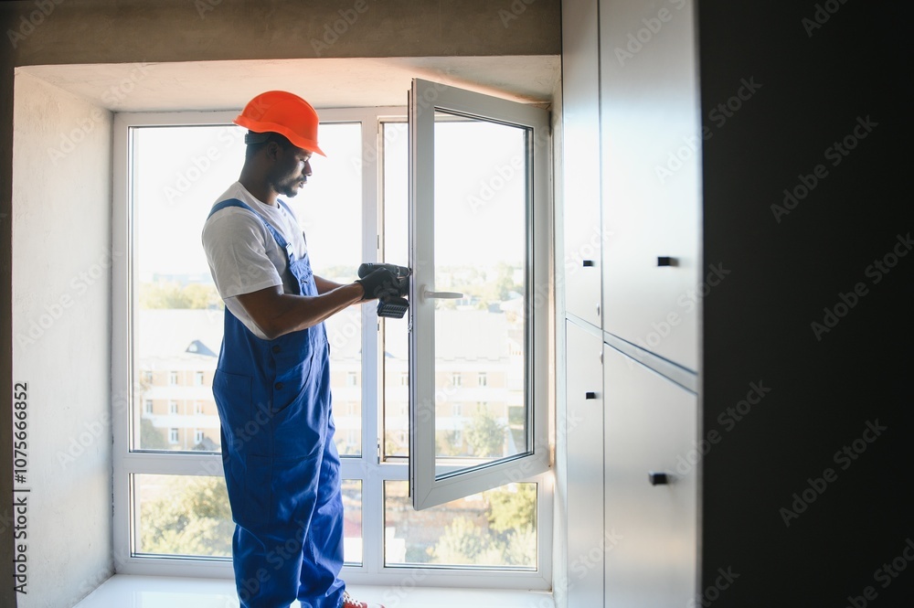 Workman in overalls installing or adjusting plastic windows in the living room at home Workman in overalls installing or adjusting plastic windows in the living room at home