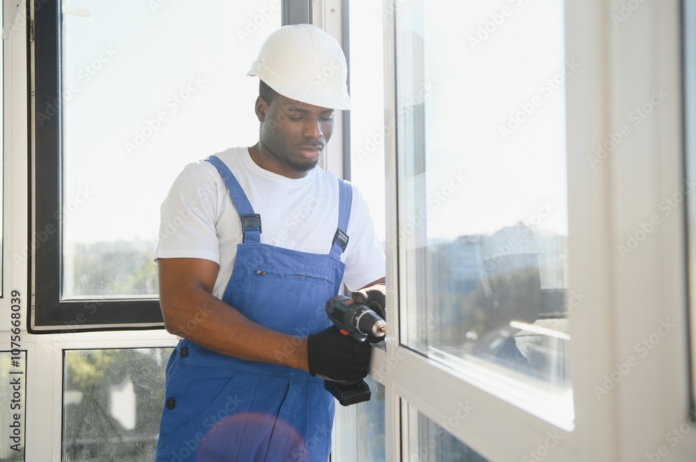 Workman in overalls installing or adjusting plastic windows in the living room at home Workman in overalls installing or adjusting plastic windows in the living room at home