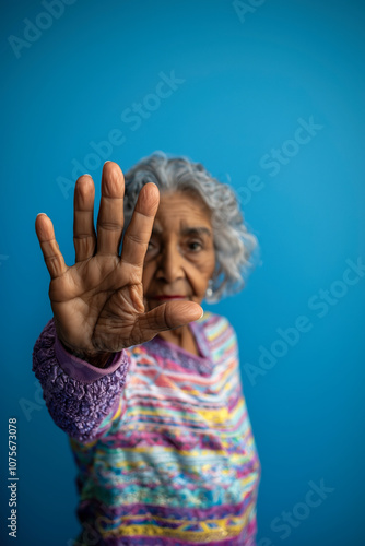 Elderly woman raising her hand in a gesture symbolizing resistance and demand for respect, highlighting awareness of elder abuse. The blue background accentuates her call for dignity and rights. photo