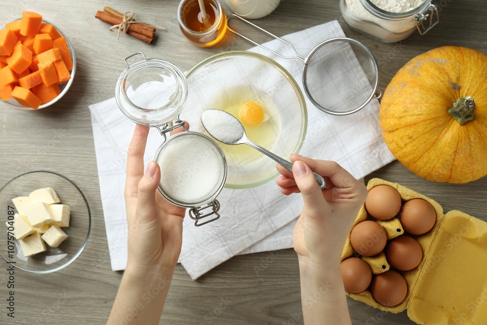 Making pumpkin pancakes. Woman adding sugar to eggs at wooden table, top view Making pumpkin pancakes. Woman adding sugar to eggs at wooden table, top view