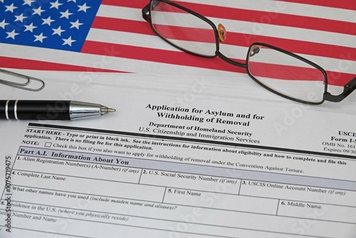 USA Application for Asylum and for Withholding of Removal paperwork, issued by U.S. Citizenship and Immigration Services under the Department of Homeland Security, is shown with an American flag. photo