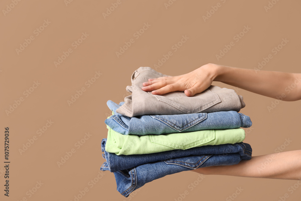 Fototapeta premium Female hands with stack of different jeans on beige background