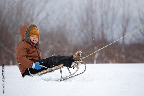 A happy child on a towed sled plunges into the deep snow, it is difficult to pull, but child to have fun
