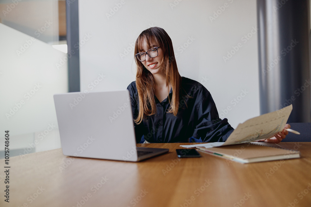 A focused woman in a chic and stylish office space, diligently working on her laptop with important documents at hand A focused woman in a chic and stylish office space, diligently working on her laptop with important documents at hand