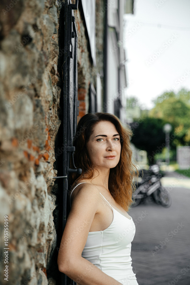 Fototapeta premium Woman in white dress leaning on stone wall outdoors
