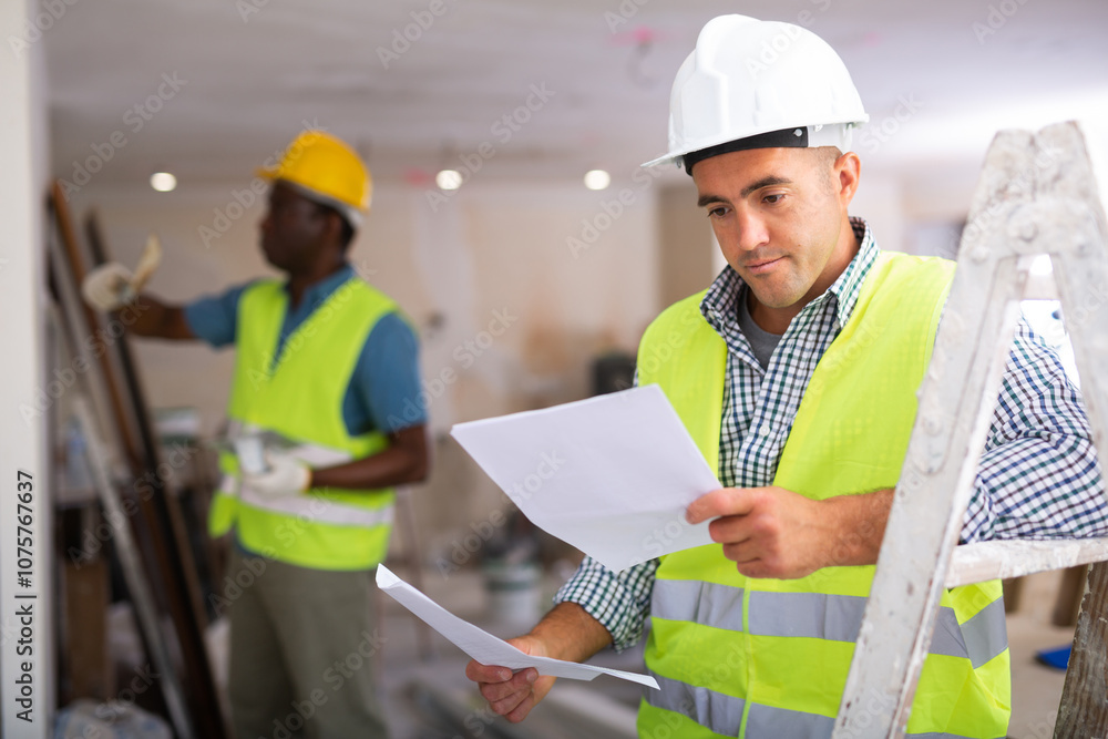 Portrait of foreman with documents analyzing plan of renovation works in apartment. Portrait of foreman with documents analyzing plan of renovation works in apartment.