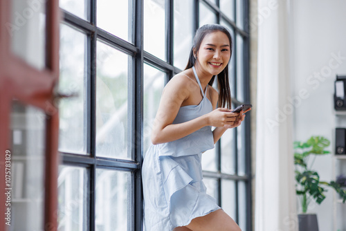 Cheerful beautiful Asian woman holding smartphone in the office workplace, 