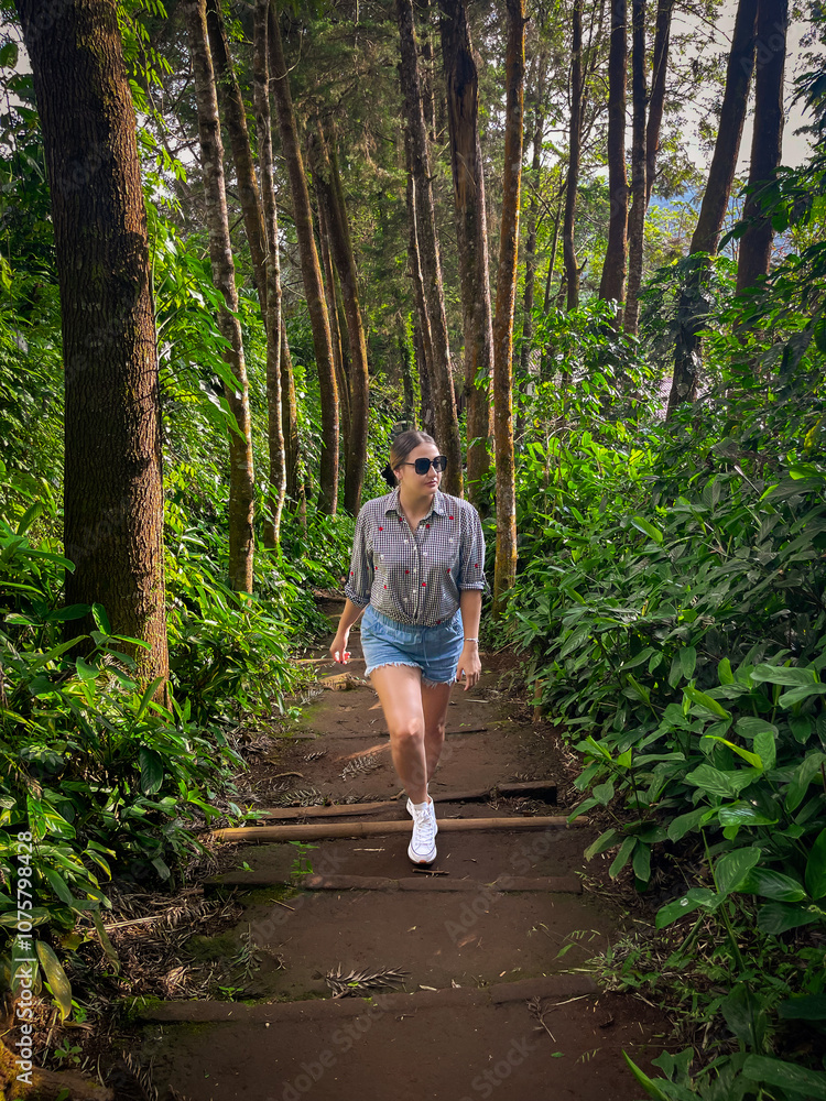 Fototapeta premium Beautiful Young woman walking up the stairs in the forest, wearing a shirt and shorts. Travel concept. Outdoor lifestyle portrait.
