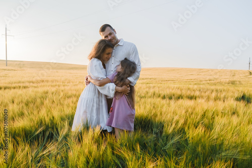 Farmer family with little daughter walking through wheat field. Mom dad boy walking together holding hands. Father mom little son walking through wheat field against blue sky. Parents daughter.