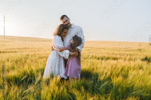 Farmer family with little daughter walking through wheat field. Mom dad boy walking together holding hands. Father mom little son walking through wheat field against blue sky. Parents daughter.