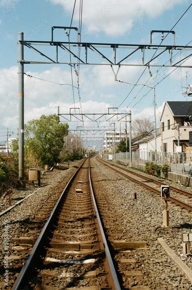 Fototapeta premium A long stretch of railway tracks in an urban area, framed by overhead electric wires and signaling equipment. The tracks extend into the distance, creating a sense of depth and perspective. 