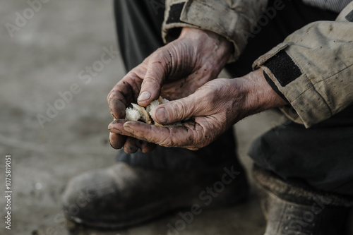 Dirty working hands of a worker on the ground. A man holds pieces of bread in his hands. The concept of hard work and result.