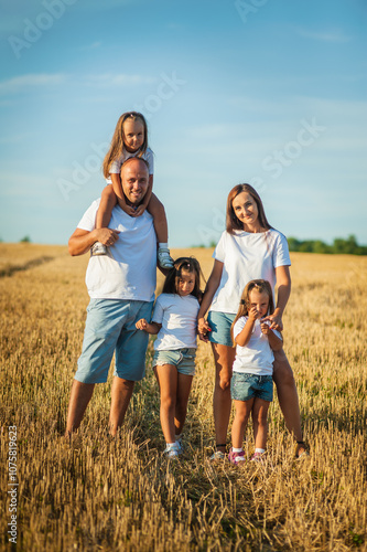 Mom, dad and  сute daughters hug in a wheat field. Beautiful children.Family vacation.Happy family resting in summer field.Cheerful family picnicking in the park.Summertime and vacation concept.