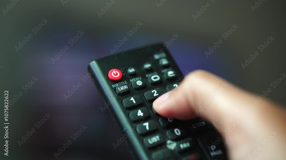 Hand holding TV remote and pressing number buttons. Focus selected. Background and foreground blur Hand holding TV remote and pressing number buttons. Focus selected. Background and foreground blur