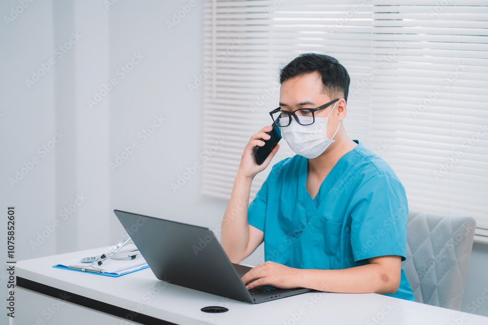 A Young Asian male doctor with glasses sitting at desk, looking at screen, working intently on laptop in office. Professional therapist writing report or email, Work stress