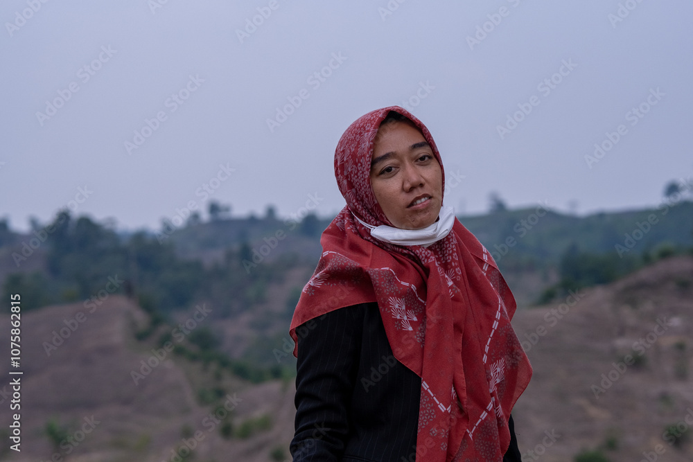 Woman on a hillside, looking contemplative, surrounded by nature's calm beauty, wrapped in a red headscarf. Woman on a hillside, looking contemplative, surrounded by nature's calm beauty, wrapped in a red headscarf.