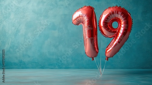 Red foil balloons in the shape of the number 19, floating against a turquoise wall. photo