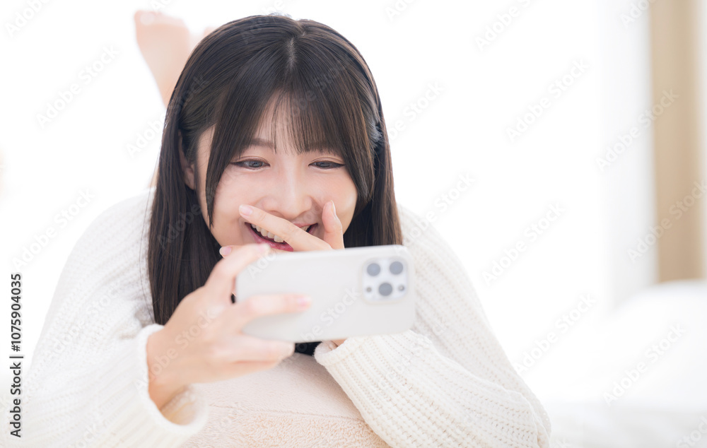 Closeup of a young woman lying face down, watching a video on her phone, in a fun, happy mood tapping away. Copy space to the right. Closeup of a young woman lying face down, watching a video on her phone, in a fun, happy mood tapping away. Copy space to the right.