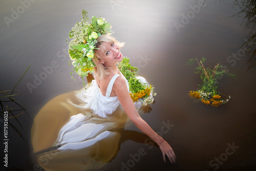 A girl in a white sundress, a wreath of flowers and a bouquet in the water in the evening at sunset. The Slavic Holiday of Ivan Kupala