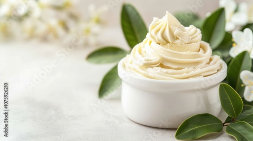 A creamy, swirled butter or frosting in a white bowl, surrounded by fresh leaves and flowers, creating a serene, elegant aesthetic.