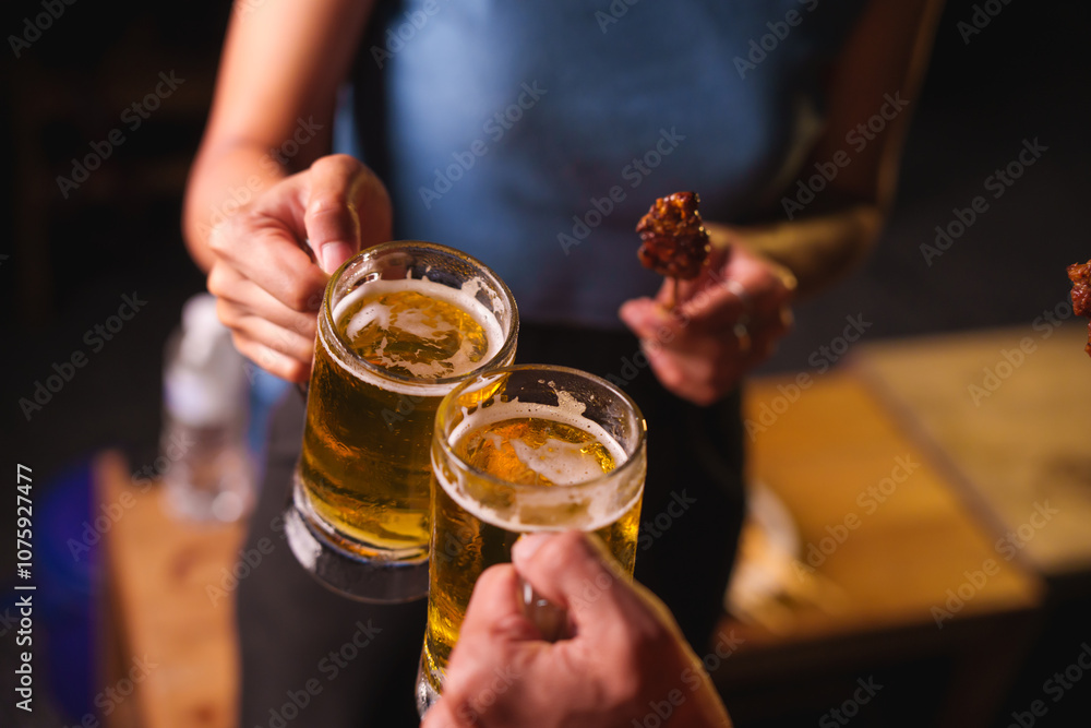 Close-up of friends clinking glasses of beer, celebrating together at a bar.The lively atmosphere captures laughter, camaraderie,good times, as young friends enjoy a night out with refreshing drinks Close-up of friends clinking glasses of beer, celebrating together at a bar.The lively atmosphere captures laughter, camaraderie,good times, as young friends enjoy a night out with refreshing drinks
