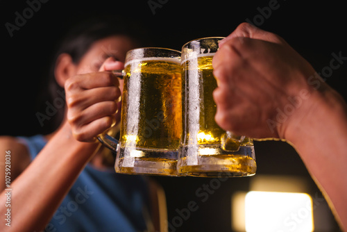 Close-up of friends clinking glasses of beer, celebrating together at a bar.The lively atmosphere captures laughter, camaraderie,good times, as young friends enjoy a night out with refreshing drinks