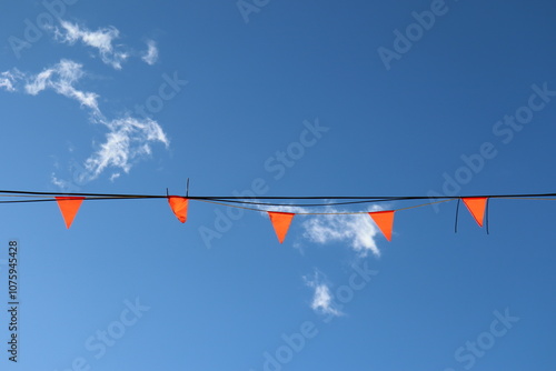 A blue sky with little and orange flags. Lifestyle and sinplicity. Day and weather. Blue and orange background. Happiness and outdoor activities.  photo