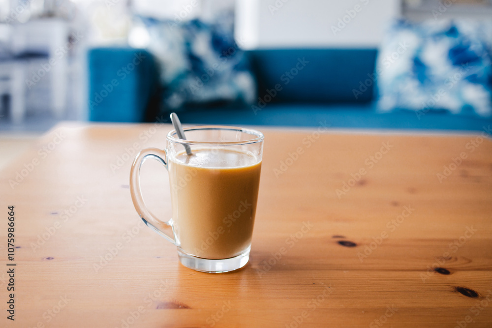 hand holding coffee in clear mug in front of blurred home interior background, habits and lifestyle concept hand holding coffee in clear mug in front of blurred home interior background, habits and lifestyle concept