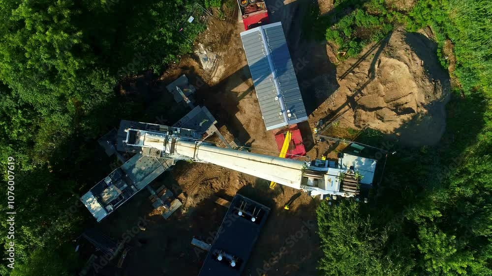 A large crane on a construction site surrounded by trees and machinery in daylight, aerial view A large crane on a construction site surrounded by trees and machinery in daylight, aerial view