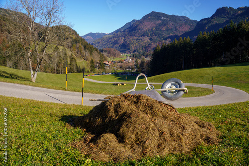 Haystack with a wheelbarrow on it. Picturesque mountain landscape with winding mountain road down to the mountaineering village of Sachrang, Bavaria, Germany. In the background the Chiemgau Alps photo