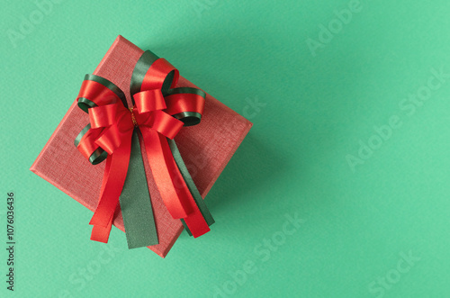 Concept for holiday and christmas. Red gift box tide red-green bow on green background. Top view, flay lay with copy space. photo