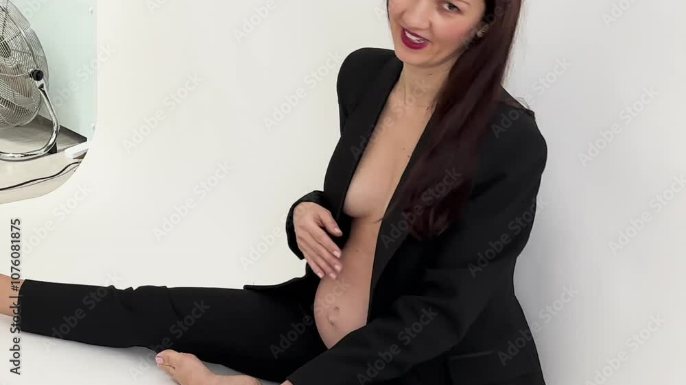View of tummy bump of a pregant woman in black blazer having her maternity shoot in studio. Woman posing. View of tummy bump of a pregant woman in black blazer having her maternity shoot in studio. Woman posing.
