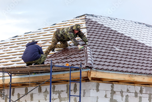 Two men are working on a roof, one of them is wearing a camouflage jacket photo