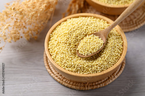 Organic yellow millet grain in wooden bowl with spoon on white table, Healthy food ingredient