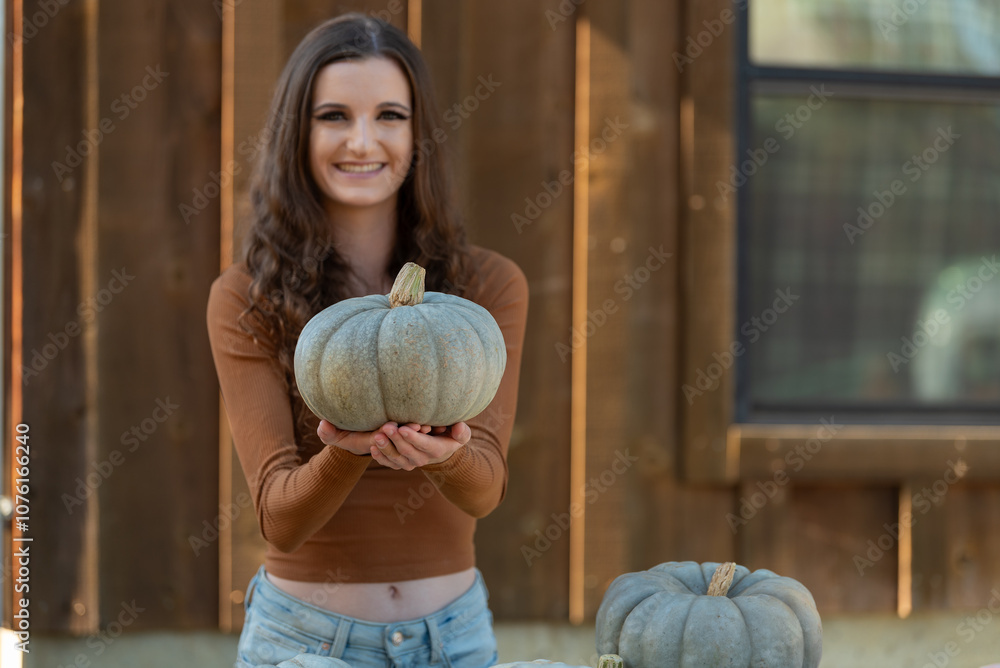 Fototapeta premium Woman holding a pumpkin at a rustic farm setting.