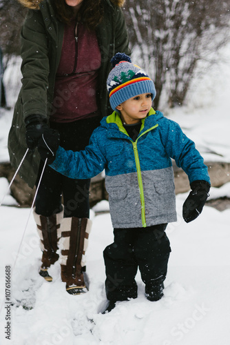 Mom helps hispanic son play in snow in winter in forest photo